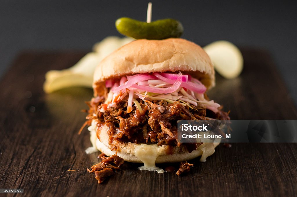 Pulled Pork Burger Slow cooked pulled pork with BBQ sauce, pickled onions, coleslaw and cheese served in a hamburger bun with dill pickle and some chips as sides. This deliciously tender and moist sandwich is perfect for lunch or dinner. Food Stock Photo