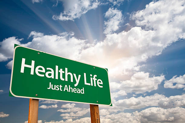 Healthy Life Green Road Sign Over Clouds Healthy Life Green Road Sign With Dramatic Clouds and Sky. health motivation stock pictures, royalty-free photos & images