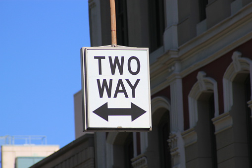 Street sign for Two Way traffic symbolized by a white sign with black letters stating TWO WAY and a thick black arrow pointing in both directions