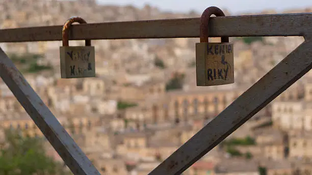 Two love locks padlocked to a fence, overlooking town of Modica in Sicily at sunset