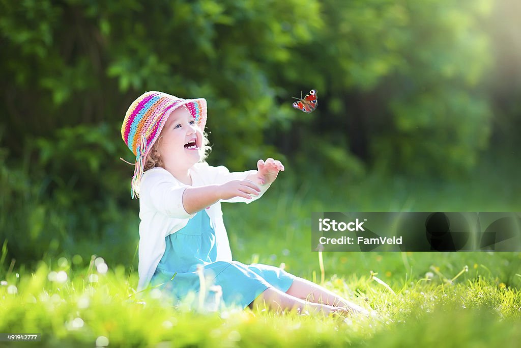 Little toddler girl playing with butterfly Happy laughing little girl wearing a blue dress and colorful straw hat playing with a flying butterfly having fun in the garden on a sunny summer day Child Stock Photo