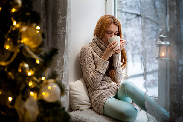 istock Young woman sitting by the window drinking hot coffee 491946624