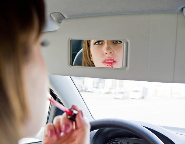 istock Young woman applying lip-gloss in car 491958153
