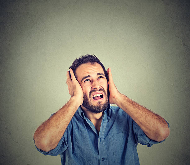 stressed man covering ears, looking up, stop making noise Portrait young annoyed, unhappy, stressed man covering his ears, looking up, to say, stop making loud noise, giving me headache isolated on grey background with copy space. Negative emotion reaction man closing ears photos stock pictures, royalty-free photos & images