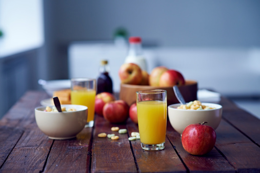 Red apples, bowls with cereal and glasses with orange juice on wooden table