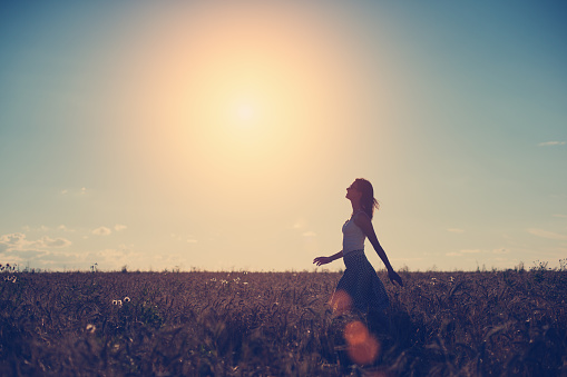 Silhouette of a girl walking in the field in the evening at sunset (intentional sun glare and vintage color)