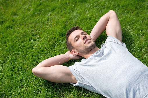 Young man relaxing at the park lying down on grass and sleeping