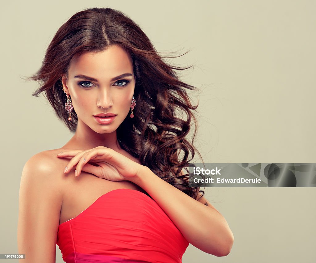 Brunette with long curled hair. Beautiful model brunette with long curled hair  in coral dress Women Stock Photo