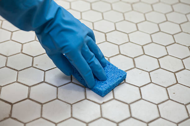 blue cleaning gloves holding a sponge cleaning a tile floor stock photo