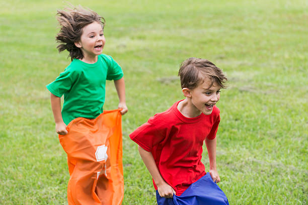 два мальчики весело конкурирующих в картофель бег в мешках - child playing sack race sports race стоковые фото и изображения