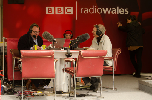 Laugharne, Carmarthenshire, Wales - May 5, 2014: Professor Wynn Thomas is interviewed about the significance of poet Dylan Thomas by Jamie Owen at a BBC Radio Wales outside broadcast at Laugharne Castle.  A producer tries to keep the banner from blowing over.