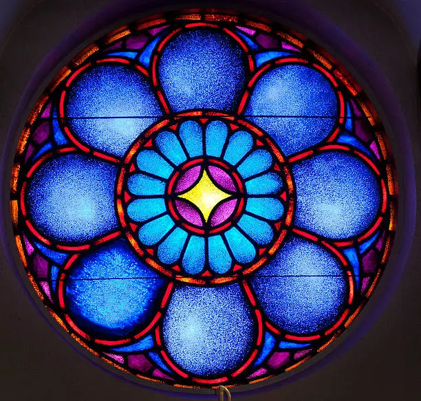 Round Stainglass window blue, red, yellow, with patterns was inside a church.