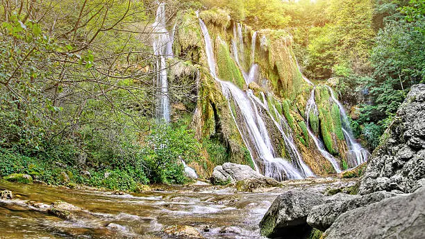 Photo of Majestic waterfall in french forest with streaming sunlight