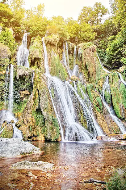 Photo of Majestic waterfall in french forest with streaming sunlight