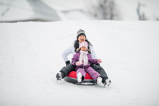 A mother and daughter are sharing an inner tube while they go sledding down a snowy hill.