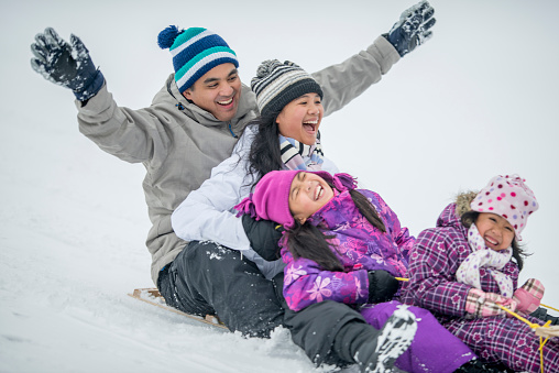 A family of four is tobogganing down a snowy hill and are laughing and smiling together.
