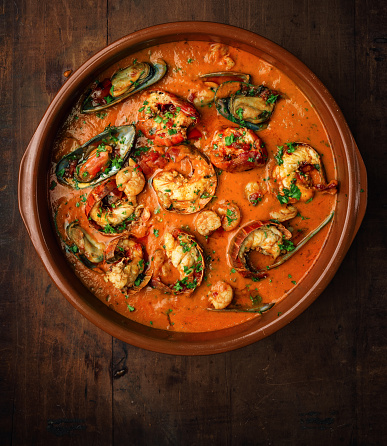 Cioppino in clay ceramic pan over wooden background