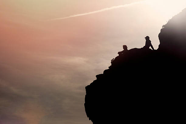 istock people silhouettes sitting on the rock at sunset 492006806