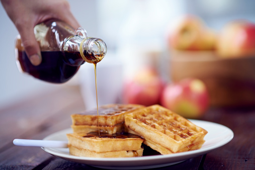 Hand pouring sweet syrup on tasty waffles