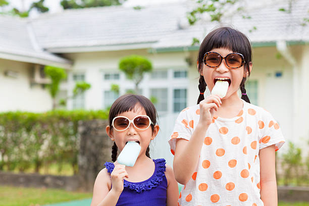 Cute little Girls Eating Ice Cream before their house Cute little Girls Eating Ice Cream before their house outside asian little chinese girls eating ice cream stock pictures, royalty-free photos & images