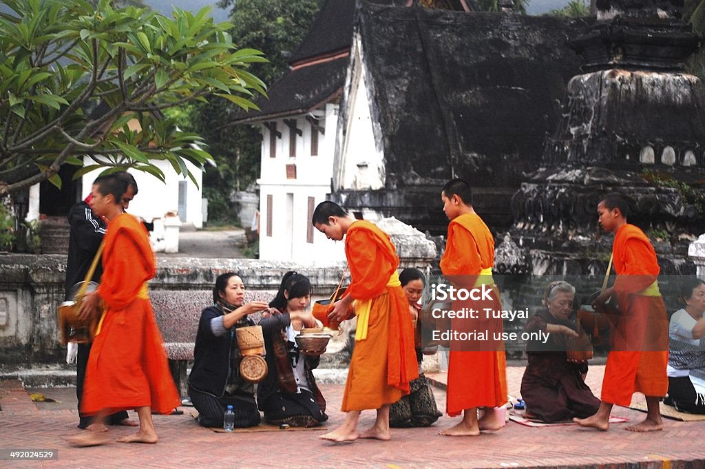 Almsgiving to put sticky rice at Luang Prabang City Loas Luang Prabang, Laos - November 2, 2011: Every day very early in the morning, the monks walk the streets to beg almsgiving food offerings to a Buddhist monk in Luang Prabang, Laos. Adult Stock Photo