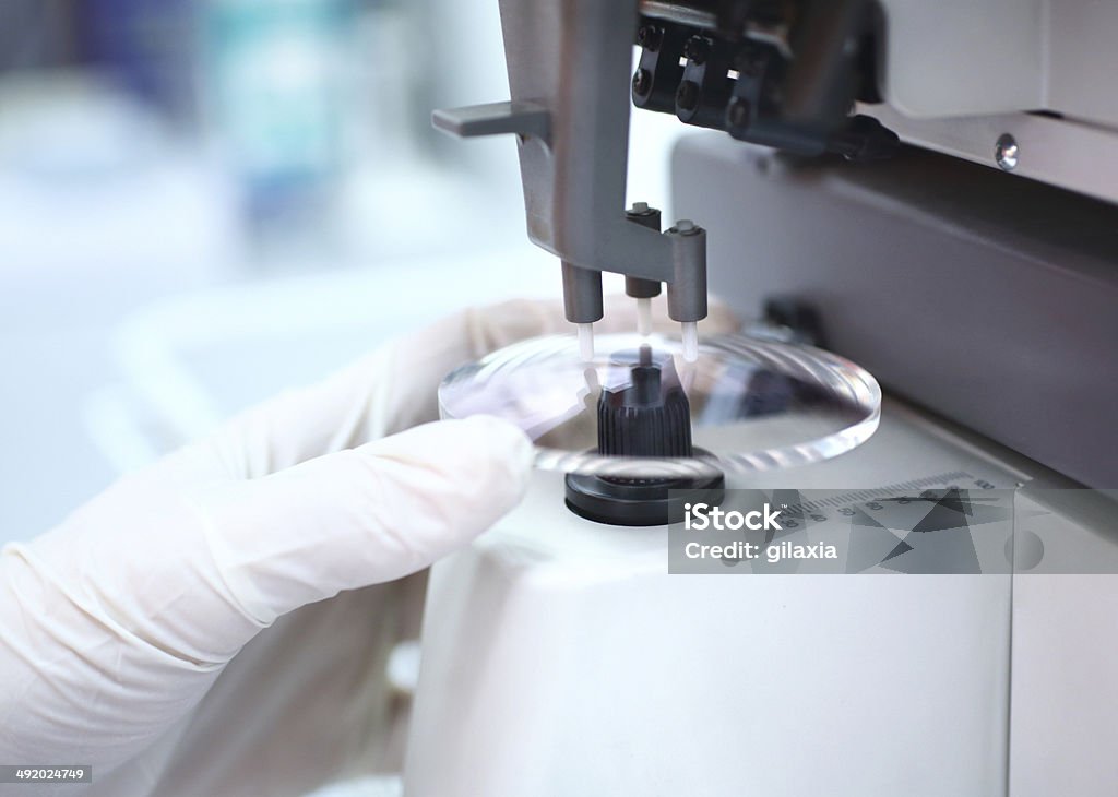 Eyeglasses production. Closeup of unrecognizable caucasian technician's hand placing piece of lens glass into machine that will mark the focal center before sending it to glass grinder. The technician is wearing white protective gloves. Lens - Optical Instrument Stock Photo