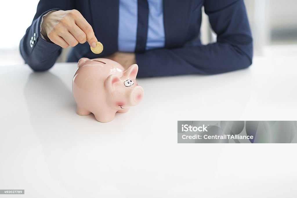 closeup on business woman putting coin into piggy bank Closeup on business woman putting coin into piggy bank Adult Stock Photo