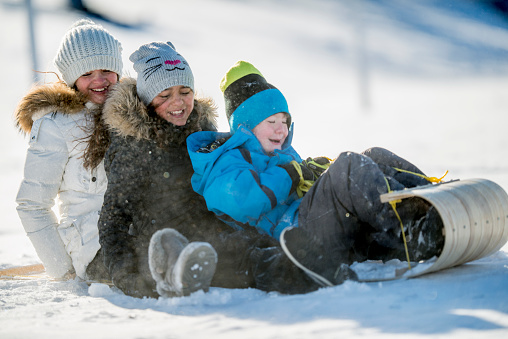 A group of children are sledding on a snowy hill. They are sitting on a toboggan on a beautiful sunny day.