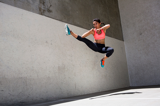 Portrait of an attractive brunette young woman athlete doing a power jump in the air against a grey concrete background.