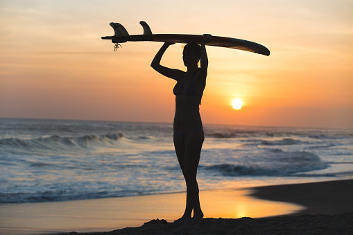 Beautiful young surfer girl in bikini with surfboard on a beach