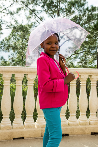 A young African American girl posing int he rain with an umbrella.