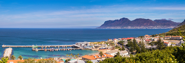 Kalk Bay landscape panorama seen from mountain side above, with false bay and Fish Hoek below the mountains above. Kalk Bay is a popular tourist destination where the fishing boats sell fresh fish as they arrive from their fishing catch.