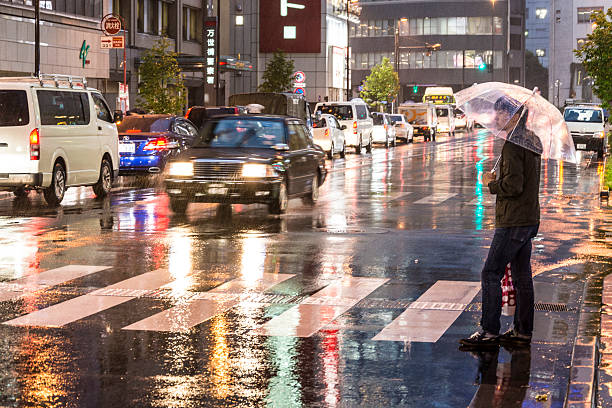Tokyo, Japan - October 1, 2015: A young man with an umbrella waits to cross a road in Akihabara district of Tokyo. Cars and signs in the background.