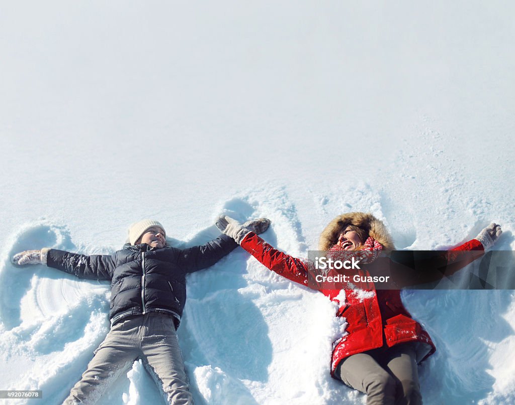Happy mother, son playing having fun lying in snow winter Happy mother and son playing and having fun together lying in the snow on a sunny winter day Winter Stock Photo