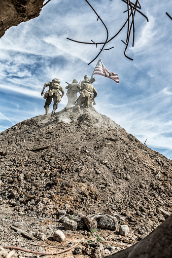 A World War II US Army military infantry platoon squad has just burst out of a culvert pipe to storm up this hill and claim it symbolically by planting an American flag at the peak.