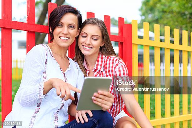 Happy Girls In The Park Using Digirtale Tablet Stock Photo - Download Image Now - 20-29 Years, 2015, Adult
