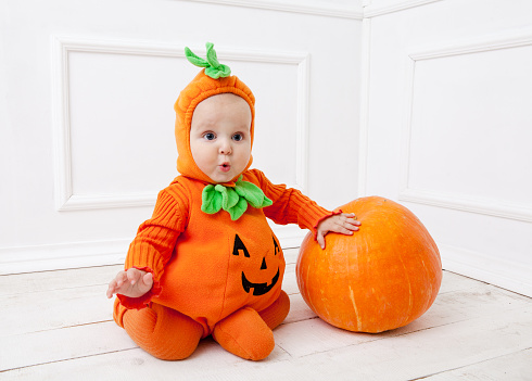 Child in pumpkin suit on white background with pumpkin