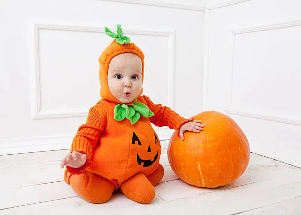 Photo of Child in pumpkin suit on white background with pumpkin