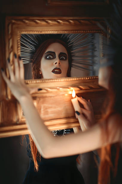 The strange goth girl holding candle in hand and looking into the mirror