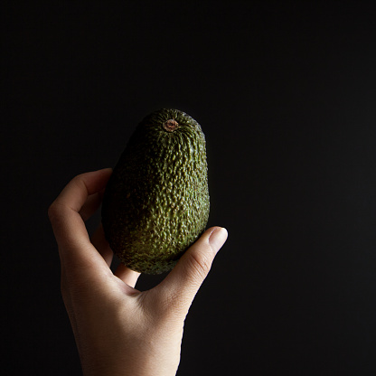 Small avocado in female hand against black background