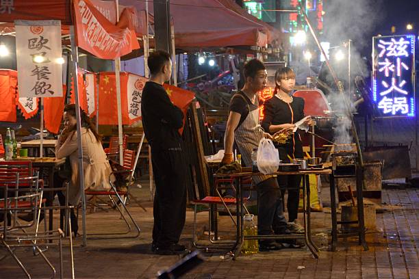 Hohhot, China - October 7, 2014: Locals in front of open restaurant with barbecue grill at a food street in Hohhot, the capital of Inner Mongolia