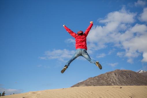 Young cheerful man in desert jumping high up in the air. 