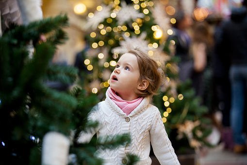 Excited little girl with open mouth looking at the beautifully decorated christmas trees with lights in the shopping mall