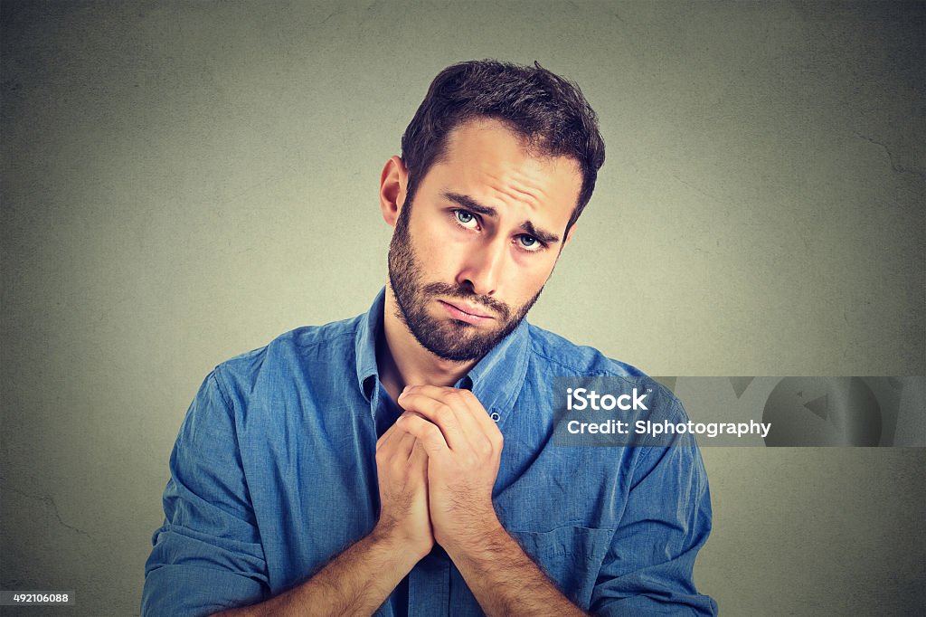 desperate man showing clasped hands asking help forgiveness Closeup portrait of desperate young man showing clasped hands, pretty please with sugar on top isolated on gray wall background. Human emotion facial expression feelings, body language Begging - Social Issue Stock Photo