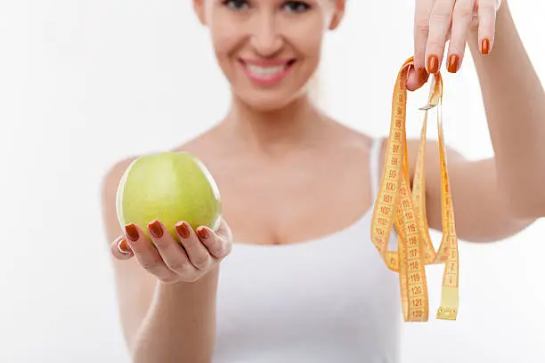 Close up of attractive slim girl is holding healthy apple and tape-line. She is showing it with proud and smiling. The lady is dieting successfully. Isolated and focus on female hands