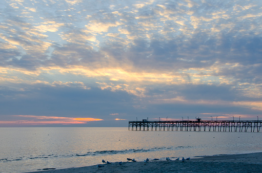 The winter sunset on Long Beach, North Carolina is filled with color and cloudscapes, silhouetting the pier on Oak Island.