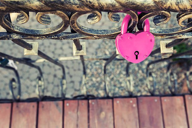Image of pink heart lock attached to the black metal grating.