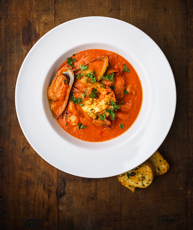 Cioppino in white elegant plate over wooden background