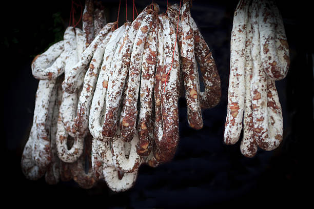 italiano stagionato salsicce e salame appesi contro sfondo nero - salami chorizo sausage sopressata foto e immagini stock