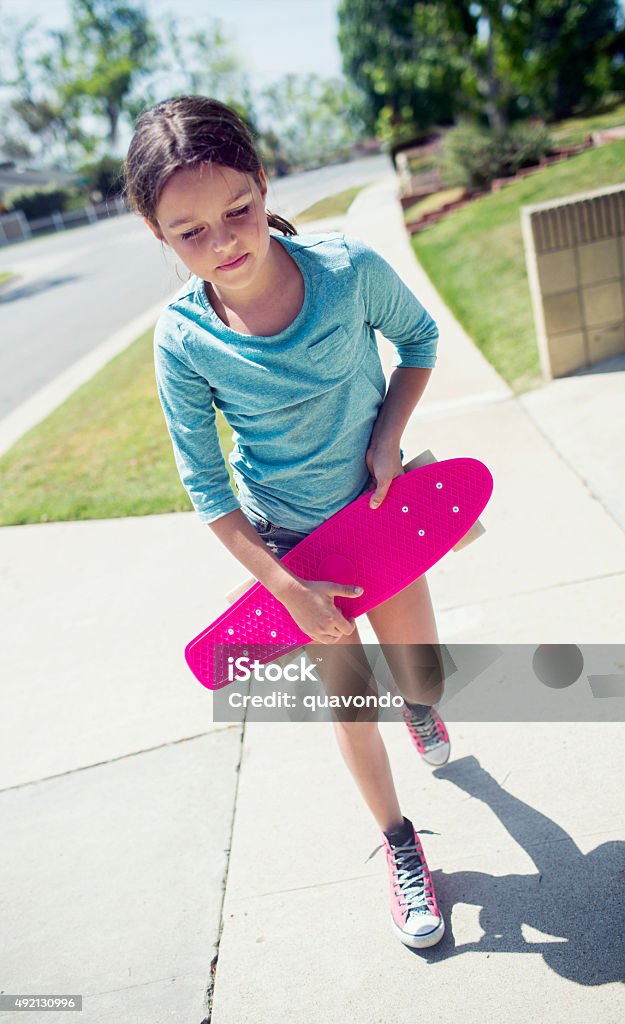 Girl walking down the sidewalk with skateboard Portrait of a girl outside walking with her pink skateboard down the sidewalk. 2015 Stock Photo